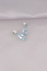 Aretes Aguamarina Corte Pera de Oro Blanco 14k, en toma de estudio, con la tela lila de fondo.