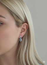 Aretes Aguamarina Corte Pera de Oro Blanco 14k, puestos en la oreja de una modelo.