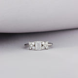 Anillo Cieli Corte Esmeralda de Oro Blanco 14k, en toma de estudio, con la tela lila de fondo.