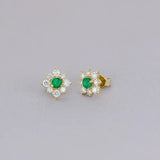 Broqueles Iris de Oro Amarillo 14k con esmeraldas, en toma de estudio sobre tela lila.