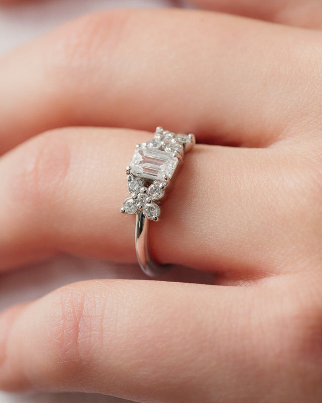 Anillo Elaine de oro blanco con diamante corte esmeralda y acentos florales, puesto en la mano