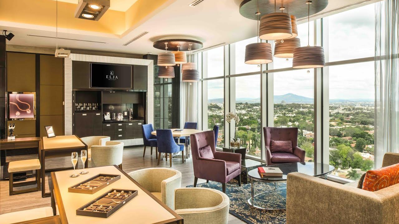 Interior del showroom de Elaine by ELJA en el Corporativo Andares, con ventanales de piso a techo y charolas de joyería sobre la mesa de atención